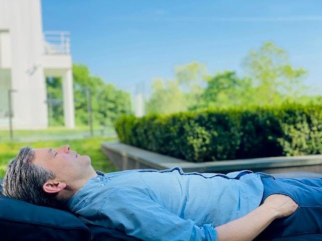 Dan Harris lying on his back outdoors with his eyes closed
